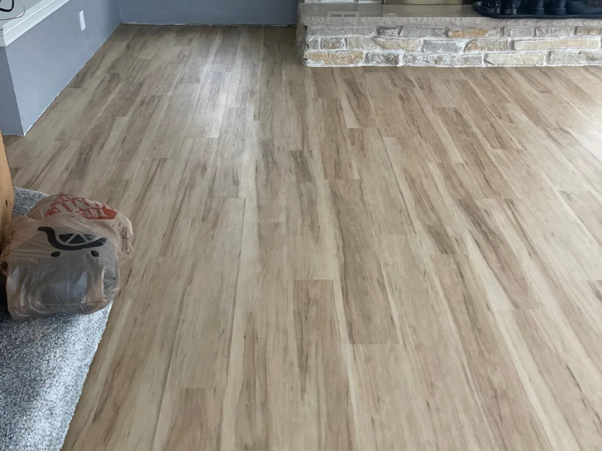 Greige vinyl plank flooring meeting a stone fireplace base and carpet transition