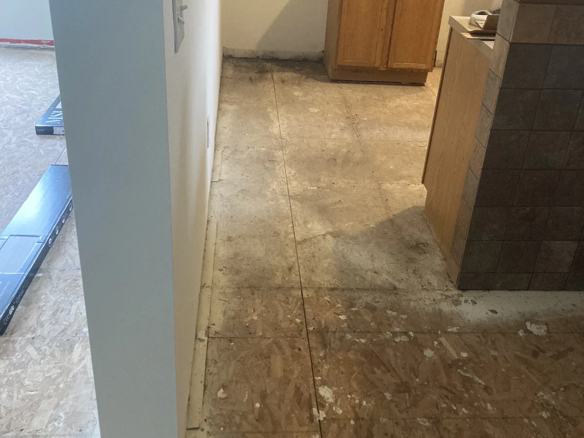 Worn subfloor exposed beside a kitchen island before new flooring is installed